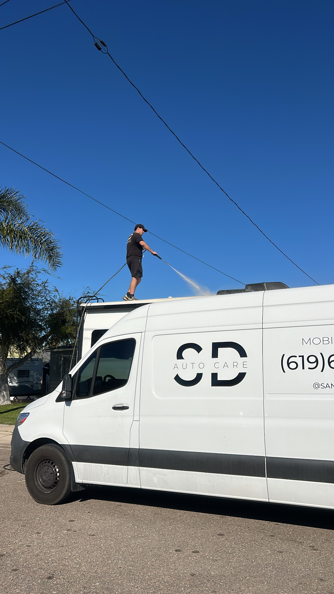 Technician washing a vehicle roof from atop the San Diego Auto Care service van